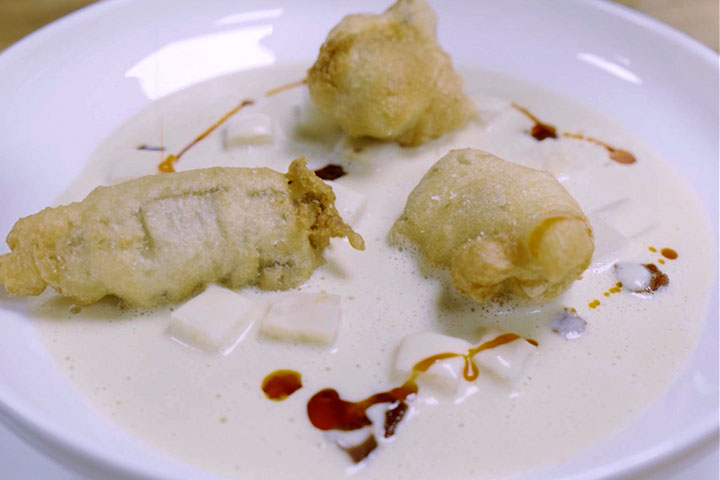Three tempura-fried oysters served in creamy oyster chowder with diced potatoes and a savory brown sauce drizzle in a white bowl