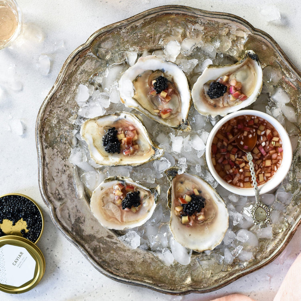 Oysters on the half shell topped with rhubarb mignonette and black caviar on crushed ice with a small bowl and spoon