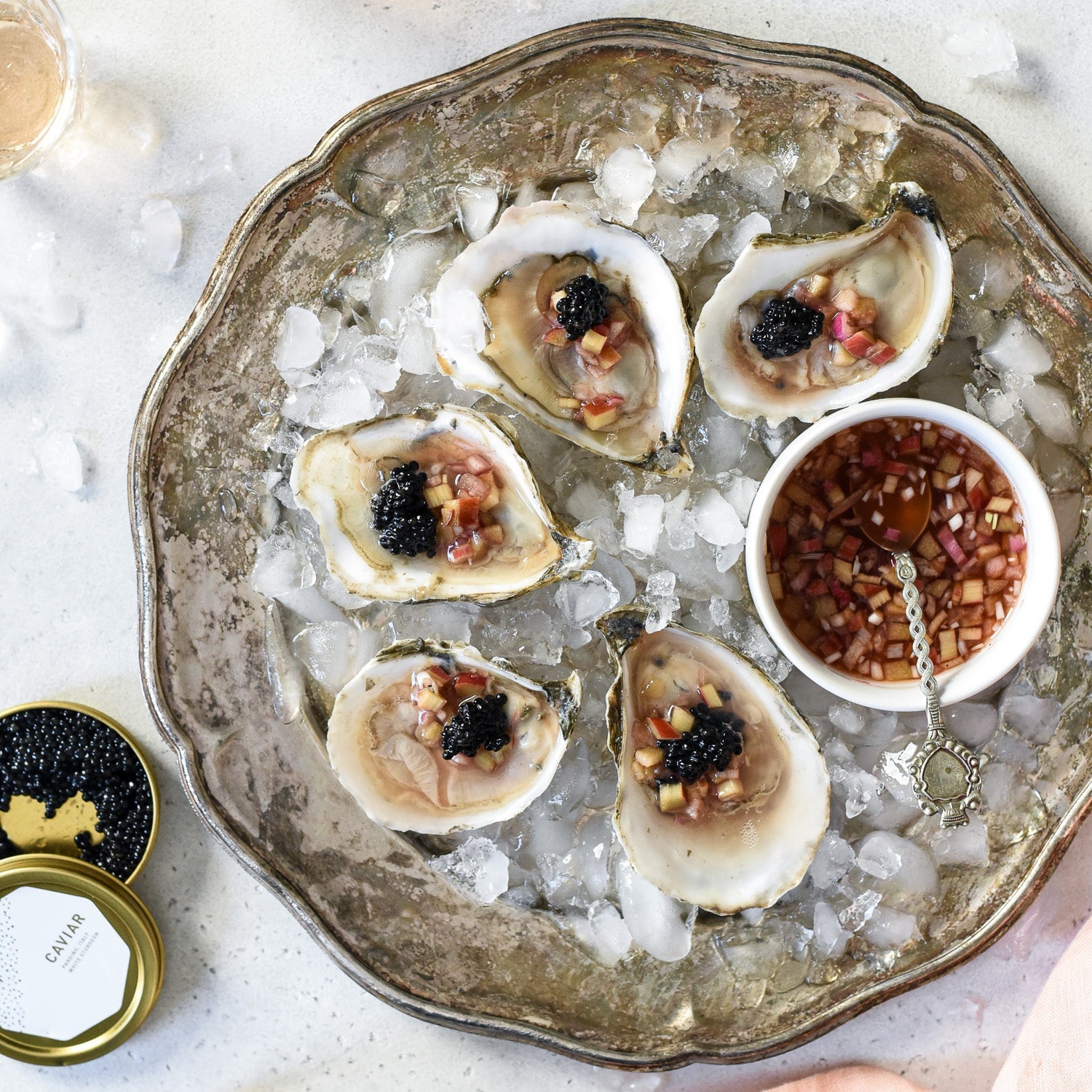 Oysters on the half shell topped with rhubarb mignonette and black caviar on crushed ice with a small bowl and spoon