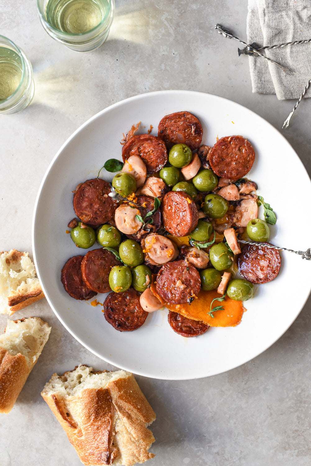 Frizzled octopus and sliced chorizo with green olives in a white bowl, drizzled with olive oil and served with crusty bread