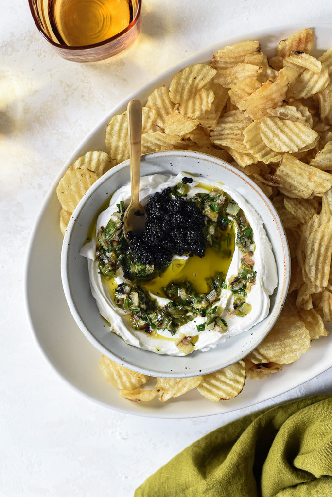 Top-down view of charred scallion labneh dip showcasing black caviar and olive oil drizzle with potato chips