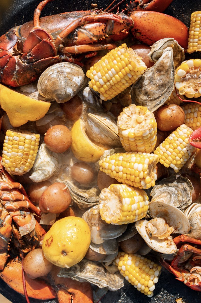 Close up of clambake with lobster, clams, oysters, corn, red potatoes and lemon steaming in a skillet