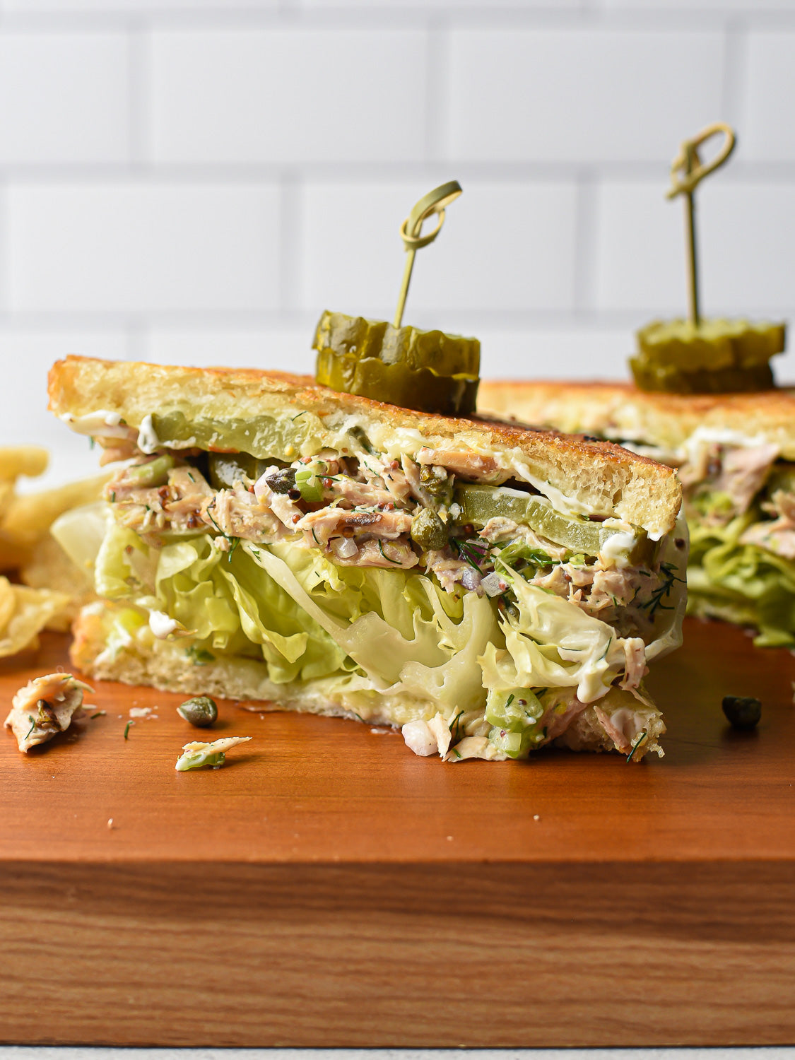 Close-up cross-section of tuna melt sandwich showing tuna salad, pickles, melted cheese, and lettuce on a wooden board