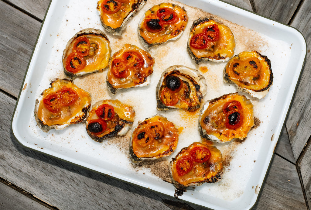 Baked oysters topped with roasted cherry tomato butter on a white enamel tray over a wooden table
