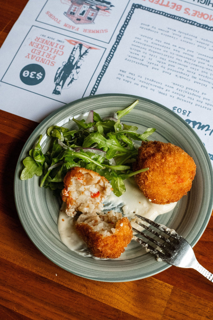 Overhead view of quahog stuffed arancini, one cut open to show filling, with creamy sauce and arugula on a green plate