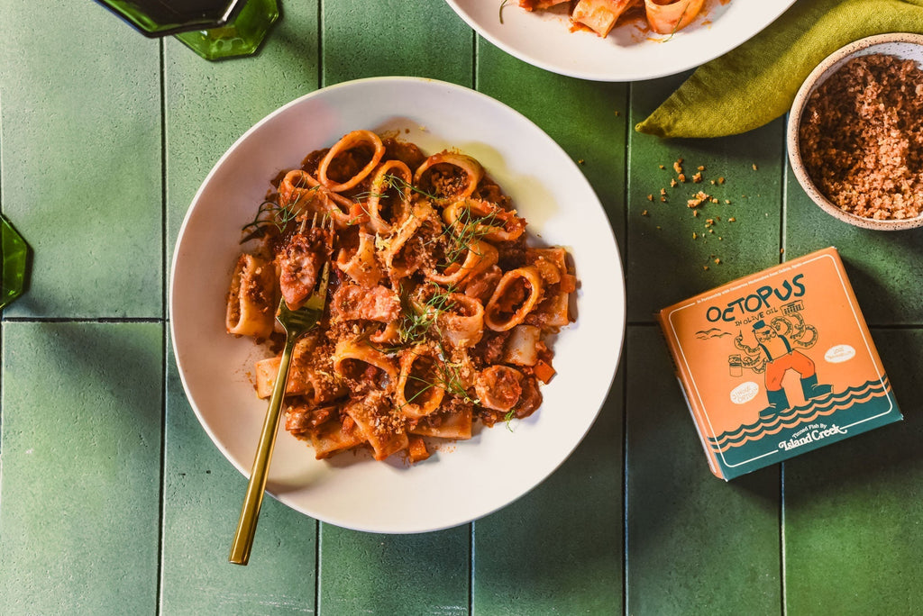 Plated octopus ragu served with fennel fronds on a green tiled table, orange Island Creek tin labeled Octopus visible at right