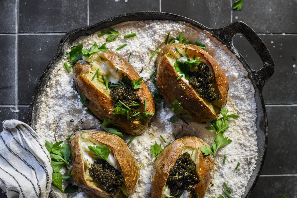 Salt-baked potatoes topped with black caviar and chopped chives served on a bed of coarse salt in a cast-iron pan