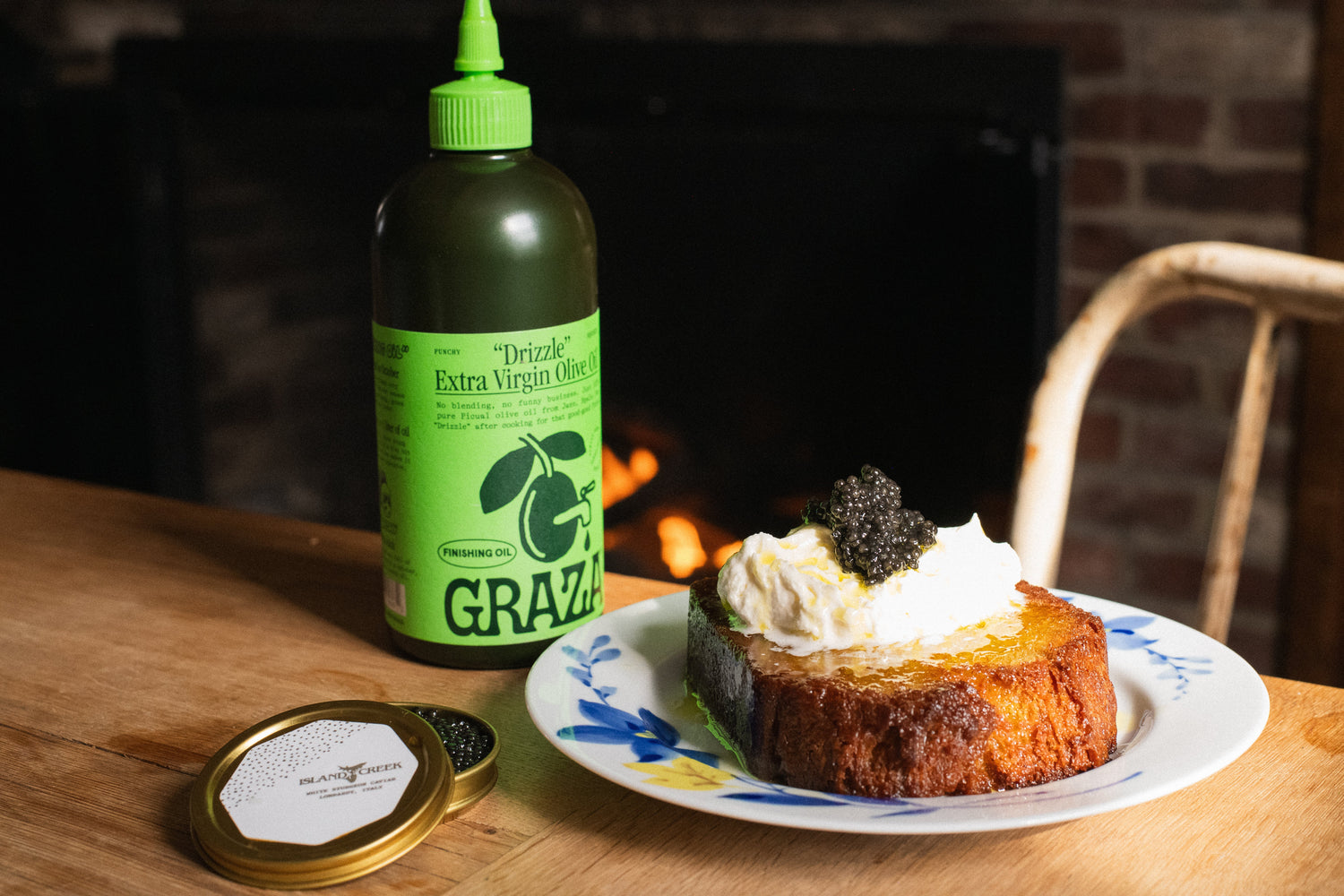Slice of olive oil cake topped with whipped cream and black caviar beside a bottle of extra virgin olive oil on wooden table